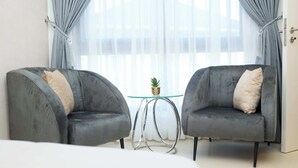 A modern room with two grey armchairs, a small glass table with a plant, and a large window with curtains. - Full Service Apartment in Cantonments, Accra. (Accra)