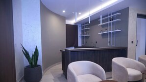 A modern interior with a curved reception desk, white armchairs, a potted plant, and a wooden coffee table. - Full Service Apartment in Cantonments, Accra. (Accra)