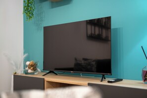 Een moderne woonkamer met een flatscreen televisie op een houten standaard, een afstandsbediening en een decoratieve schaal met gedroogde planten.