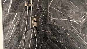 A modern shower with a handheld showerhead and a fixed wall-mounted showerhead, set against a dark marble wall with white veining. - Ocean View Retreat•4 Mn Walk 2 Beach•Lanai•Sleep 6 @ Waikiki Banyan #908 Tower 1 (Honolulu)