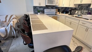A modern kitchen with a central island, white cabinets, a microwave, and a sink. - Ocean View Retreat•4 Mn Walk 2 Beach•Lanai•Sleep 6 @ Waikiki Banyan #908 Tower 1 (Honolulu)
