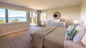 A bedroom with a large window, a bed, a dresser, and a mirror.