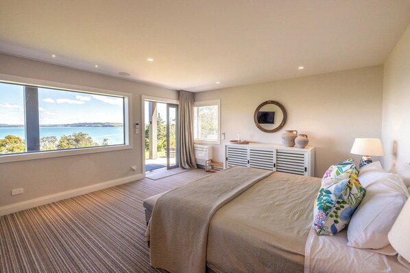 A bedroom with a large window, a bed, a dresser, and a mirror. - The Keep at Woodside Bay (Waiheke Island)