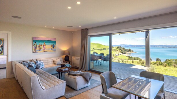 A modern living room with a large sofa, a glass coffee table, and a view of the sea.