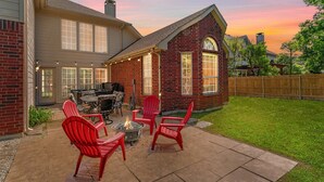 Ein Garten mit Feuerstelle, roten Adirondack-Stühlen und einem Patio-Tisch.