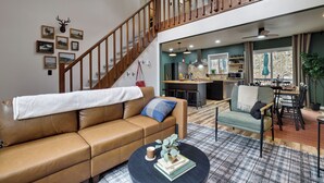 A spacious living area with a leather sofa, a coffee table, and a staircase leading to an upper level. - NEW Lodge•HotTub.Game Room.Firepit.Theater.Hammocks (Tobyhanna)