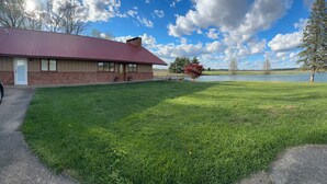 A building with a red roof and brick walls, a grassy lawn, and a body of water in the background. - Family Friendly Lakehouse with great views! (Jasper)