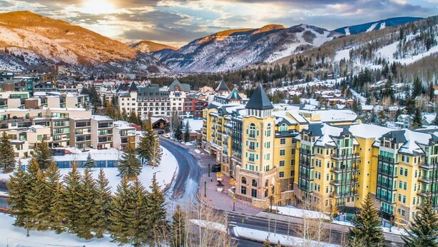 A snow-covered town with modern buildings, including a prominent yellow hotel with a green roof, surrounded by mountains and trees. - Modern 3 Bed / 3 Bath Townhome in Vail with Private Garage - Pets Welcome! (Vail)