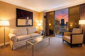 A hotel room with a sofa, armchair, and a glass coffee table. There is a large window with a cityscape view. - MGM Signature Suite • Full Kitchen • Strip View • Balcony • Pools • Gyms (Las Vegas)