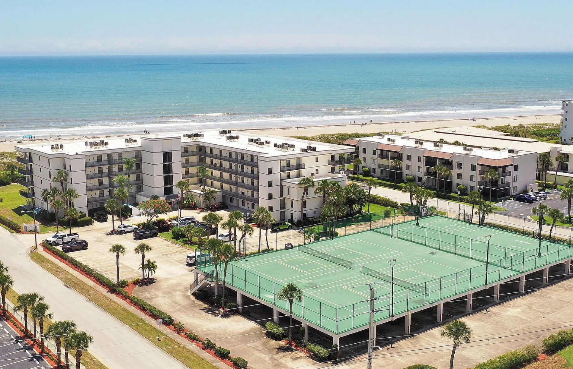 A multi-story hotel with a tennis court, parking, and a beach view.