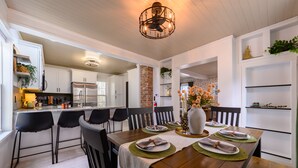 A modern kitchen with white cabinetry, a wooden dining table set for four, and a brick accent wall. - Newly Renovated | Old Town | King Suite | Fire Pit | Garage (Alpena)