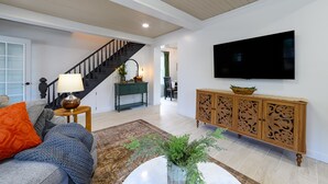 A spacious living room with a staircase, a flat-screen TV mounted on the wall, a wooden cabinet, and a comfortable seating area with a sofa and cushions. - Newly Renovated | Old Town | King Suite | Fire Pit | Garage (Alpena)