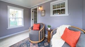 A room with a grey armchair, a grey sofa, a patterned rug, and a small wooden side table with a plant. - Newly Renovated | Old Town | King Suite | Fire Pit | Garage (Alpena)