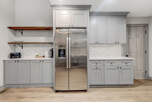 A modern kitchen with grey cabinets, a stainless steel refrigerator, a coffee machine, and a toaster. - Modern and Peaceful 5BR Wake Forest Retreat-Pet Friendly (Wake Forest)
