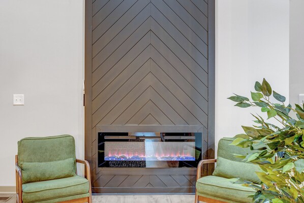 A modern living room with a fireplace, two green armchairs, and a large plant. - Modern and Peaceful 5BR Wake Forest Retreat-Pet Friendly (Wake Forest)