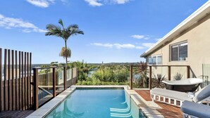 A swimming pool with a wooden deck, lounge chairs, and a view of the surrounding landscape. - Riverside Retreat with Sweeping Views – Pool, Guest Suite & Entertainers Balcony (Tweed Heads)
