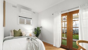 A bedroom with a bed, a window, an air conditioner, a door leading to a balcony, and a chair. - Riverside Retreat with Sweeping Views – Pool, Guest Suite & Entertainers Balcony (Tweed Heads)