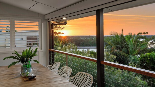 A balcony with a wooden table, white chairs, and a potted plant. - Riverside Retreat with Sweeping Views – Pool, Guest Suite & Entertainers Balcony (Tweed Heads)