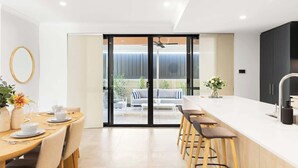Cozinha moderna com ilha central, banquetas de bar e porta de vidro deslizante que dá para uma área de estar externa.