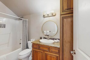 Ein Badezimmer mit Toilette, Waschbecken mit rundem Spiegel, Holzausbau und Duschvorhang.
