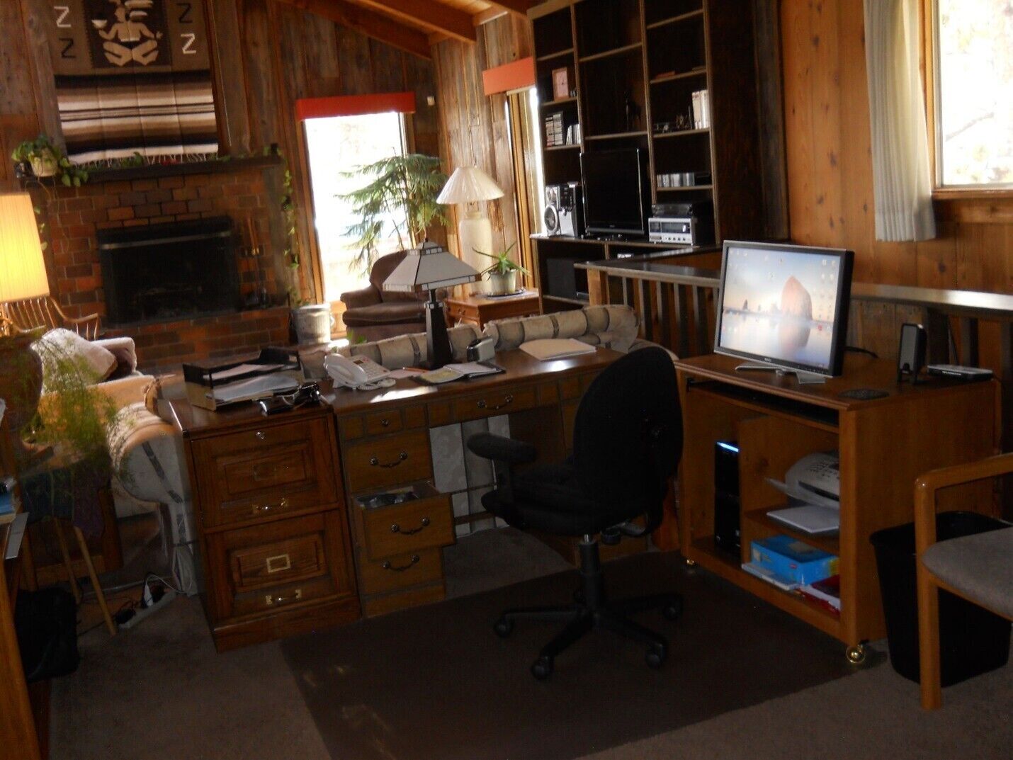 A cozy room with a fireplace, wooden shelves, a desk with a computer, and a comfortable seating area.