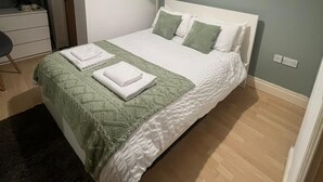 A neatly made bed with a green blanket and white pillows, a bedside lamp, and a small shelf with decorative items. - Cozy flat in Belfast (Belfast)