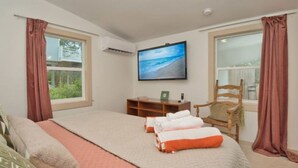 A bedroom with a bed, a TV mounted on the wall, a chair, and a window with curtains. - Quads-For-Fun, Unit 4, Saint George Island, FL (Eastpoint)