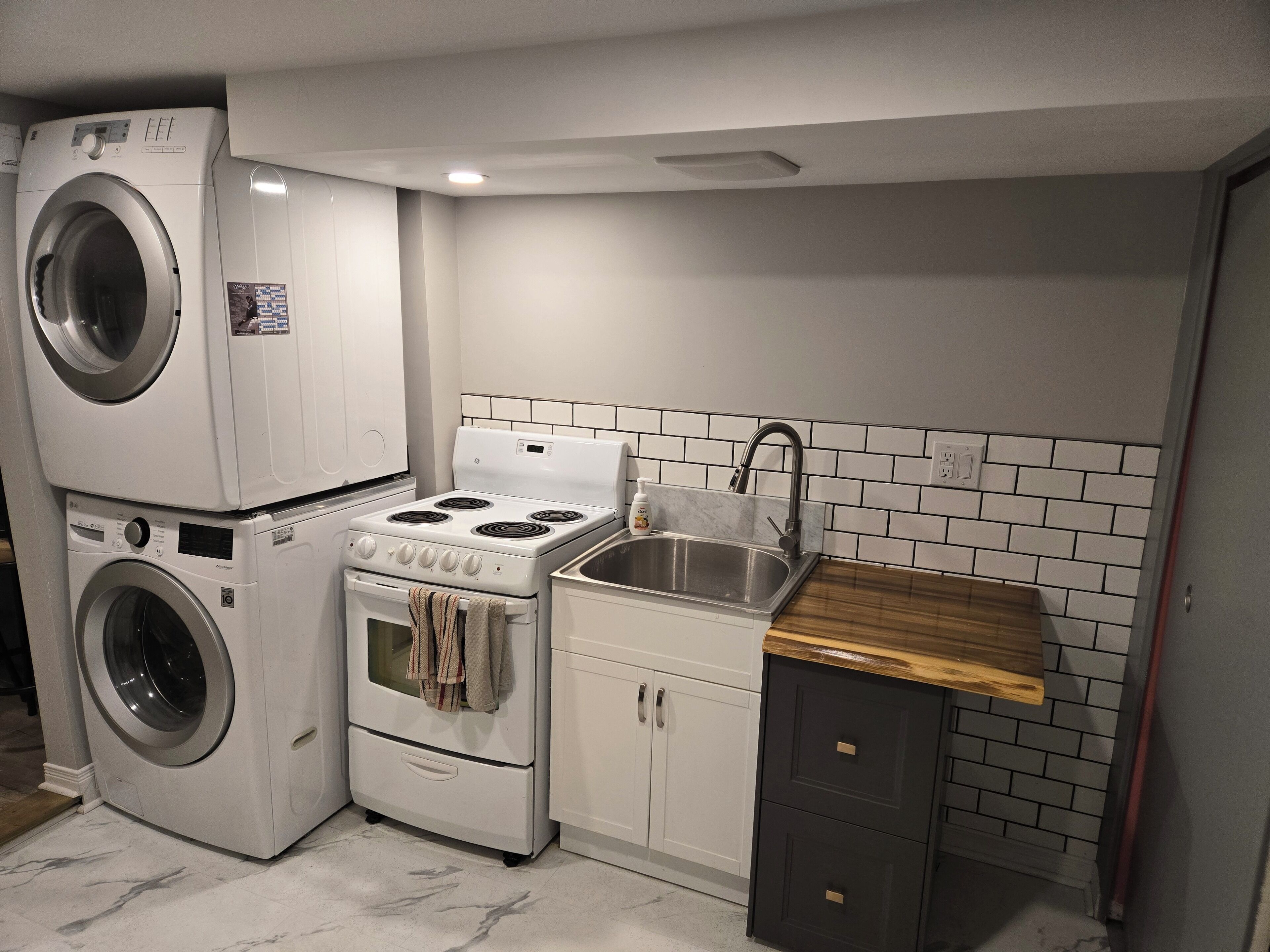 Cocina compacta con lavadora y secadora integradas, estufa, fregadero y armarios de madera.