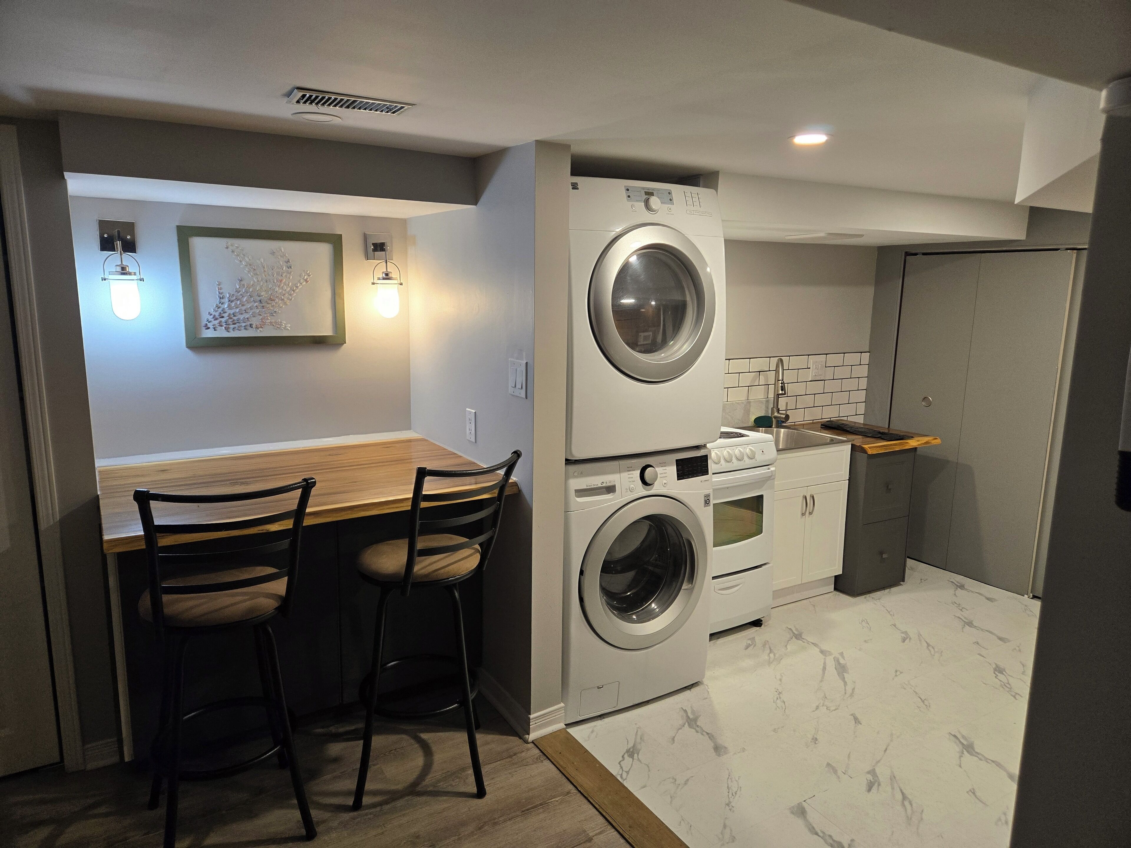 A compact laundry room with a washing machine and dryer, a wooden table with two chairs, and a tiled backsplash.