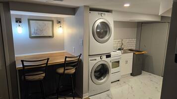 A compact laundry room with a washing machine and dryer, a wooden table with two chairs, and a tiled backsplash.