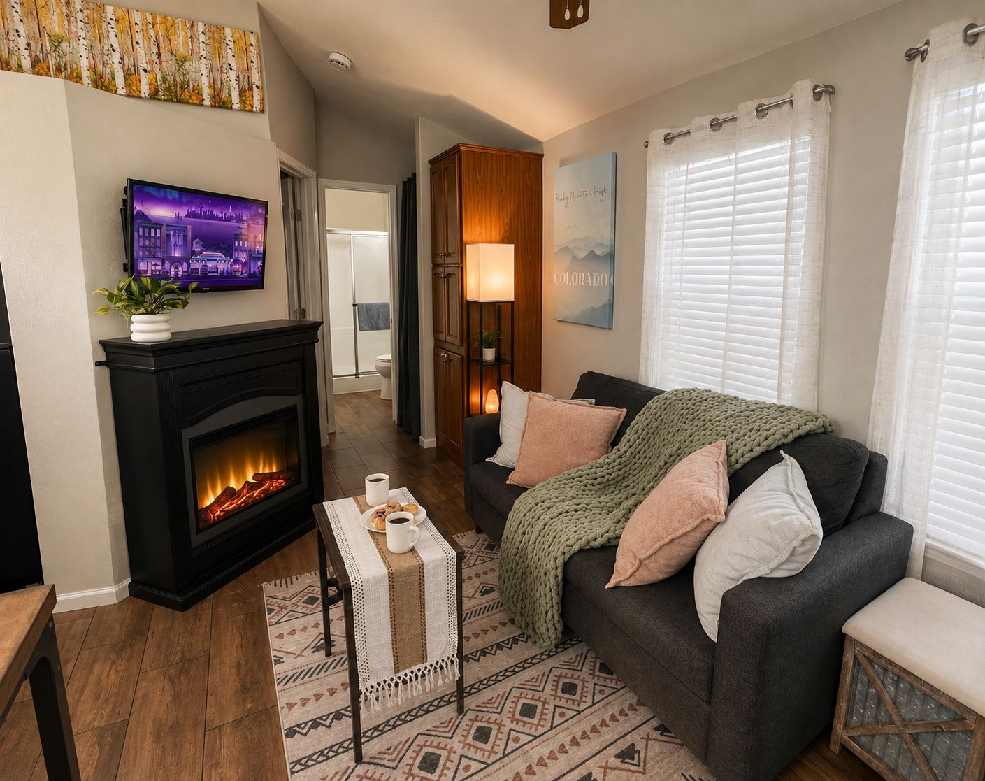 A living room with a fireplace, a television, a couch with pillows, and a window with blinds.