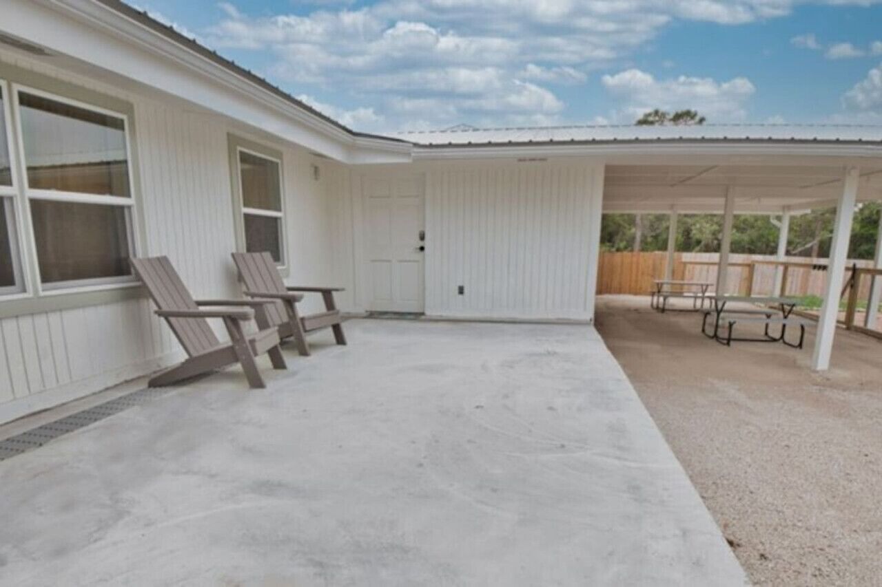 A covered patio area with concrete flooring and wooden chairs.