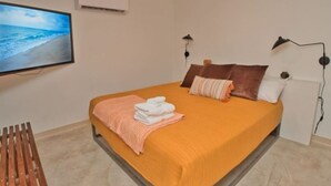 Un dormitorio con cama, televisión, aire acondicionado y un banco de madera.