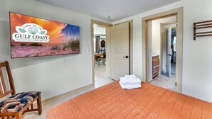 Een slaapkamer met een bed, een stoel, een televisie waarop een zonsondergang te zien is en een deur naar een andere kamer.