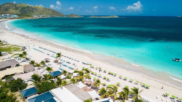 A beach with clear turquoise waters, a sandy shore, and a row of beach umbrellas.