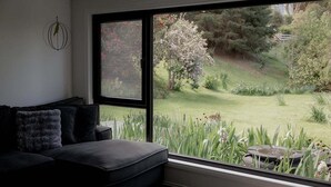Una sala de estar moderna con un ventanal grande, un sofá negro y una mesita con comedero para pájaros.