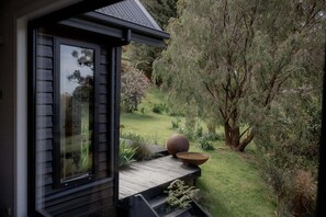 A view from a window overlooking a garden with a wooden deck, a large tree, and a spherical object on the deck. - Wilder Stay with sauna, outdoor bath and plunge (Hobart City)