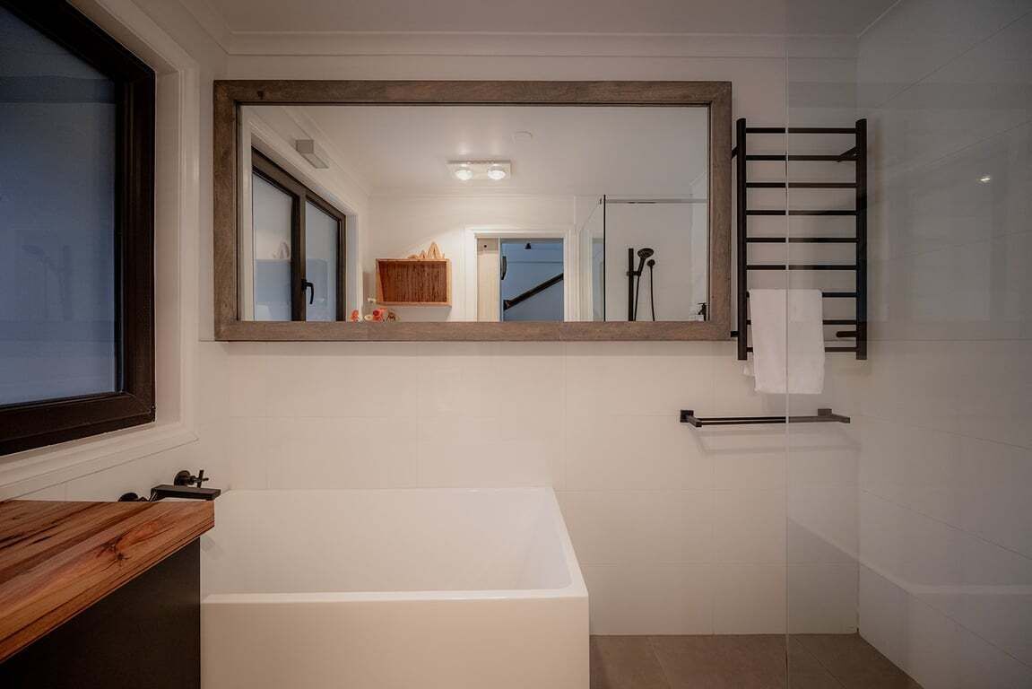 A bathroom with a large mirror, a bathtub, a towel rack, and a wooden countertop.