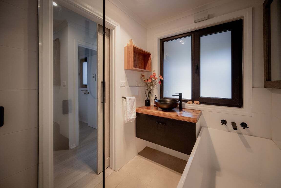 Un baño moderno con cabina de ducha de vidrio, tocador de madera, ventana grande y bañera.