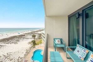 Ein Balkon mit Pool, Blick auf den Strand und zwei Stühle mit gemusterten Kissen.