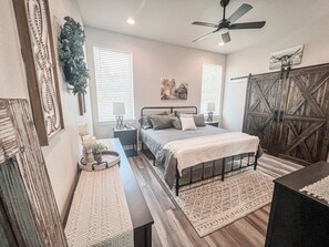Une chambre à coucher avec un lit, des tables de chevet, un ventilateur de plafond et une porte de grange au style rustique.