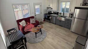 A modern kitchen with white cabinets, a stainless steel refrigerator, and a dining area with a red sofa and a small round table. - Private and charming Bay Area home. Centrally located to all Bay Area cities! (South San Francisco)