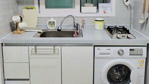A modern kitchen with white cabinets, a built-in sink, a stove, and a front-loading washing machine. - Moon Stay (Seoul)