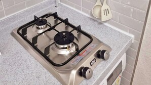 A kitchen with a gas stove, a wall-mounted thermometer, and two wooden-handled spatulas hanging on a rack. - Moon Stay (Seoul)