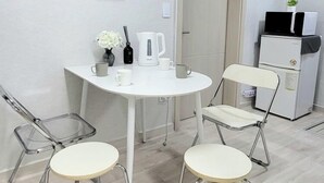 A small, modern room with a white table and two chairs, a white kettle, a coffee maker, and a refrigerator. - Moon Stay (Seoul)