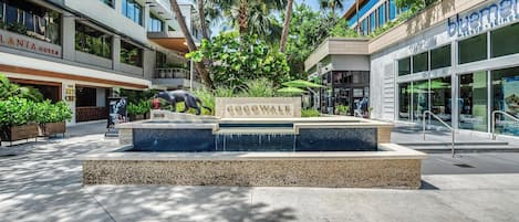 Une fontaine ornementale de Cocowalk, agrémentée d’un panneau, entourée de palmiers et de bâtiments modernes.