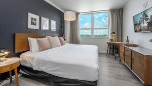 Moderni hotellihuone, jossa on suuri sänky, työpöytä ja ikkunasta avautuva näkymä kaupunkiin.
