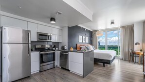 Una habitación de hotel moderna con kitchenette, cama con vistas y escritorio con silla.