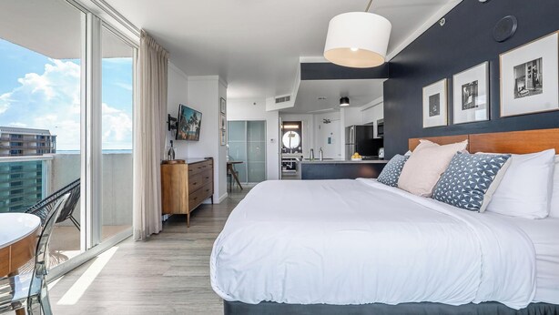 Una habitación de hotel moderna con una cama grande, un comedor, una cocina y un balcón con vistas a la ciudad.