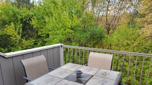 Une terrasse avec une table et deux chaises, entourée d’une rambarde et de verdure.